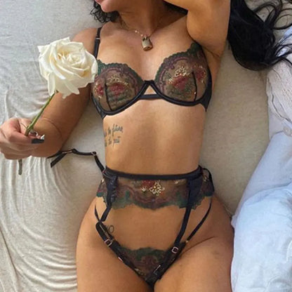 Person wearing a floral lingerie set holding a white rose on a bed.