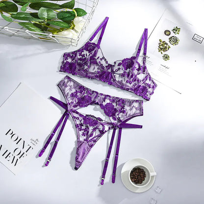 Purple lace lingerie set on a white surface with a cup of coffee and greenery.