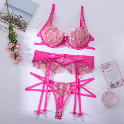 Pink lingerie set with floral details on a white surface with decorative items.