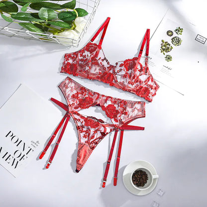 Red lace lingerie set on a white surface with a cup of coffee and green leaves.